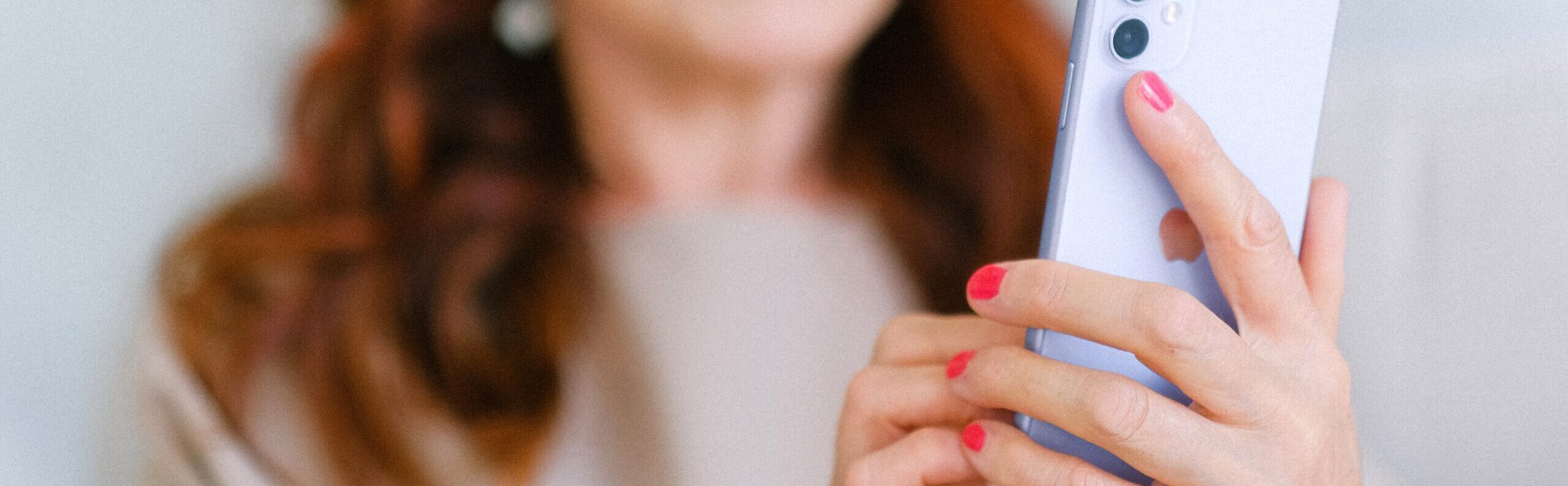 En kvinna i rött hår och rosa nagellack håller en ljuslila telefon. Telefonen är i fokus och bakgrunden suddig.